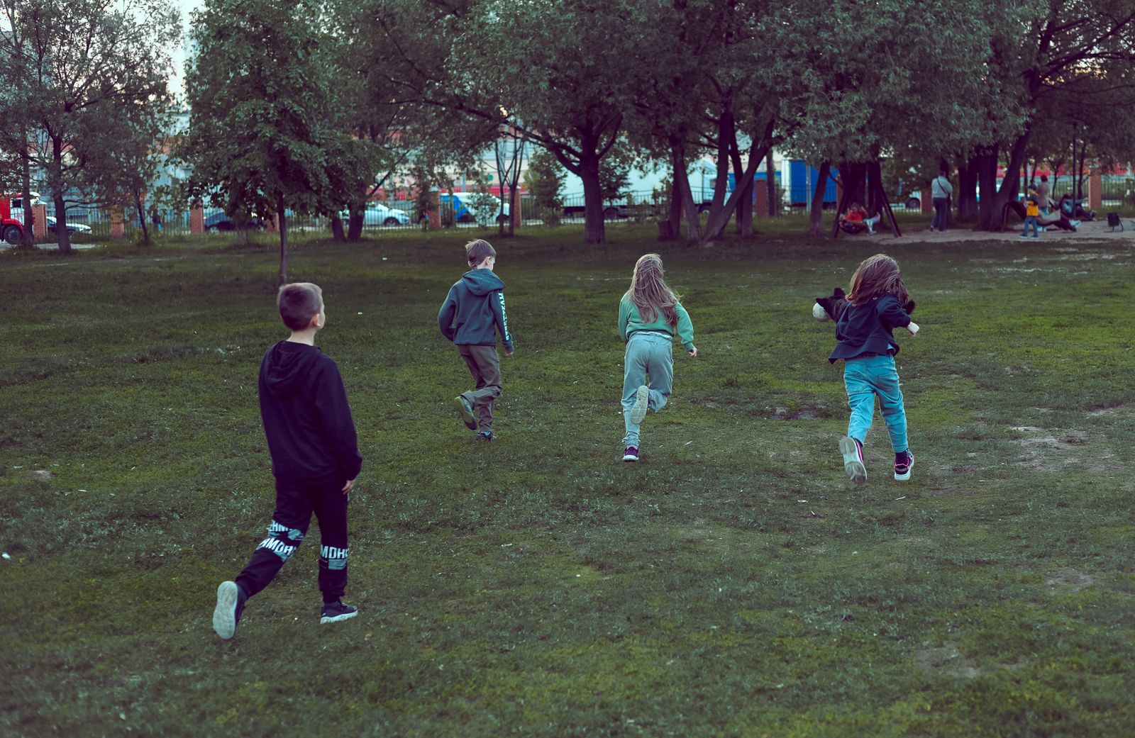 Four children running across a park towards the trees