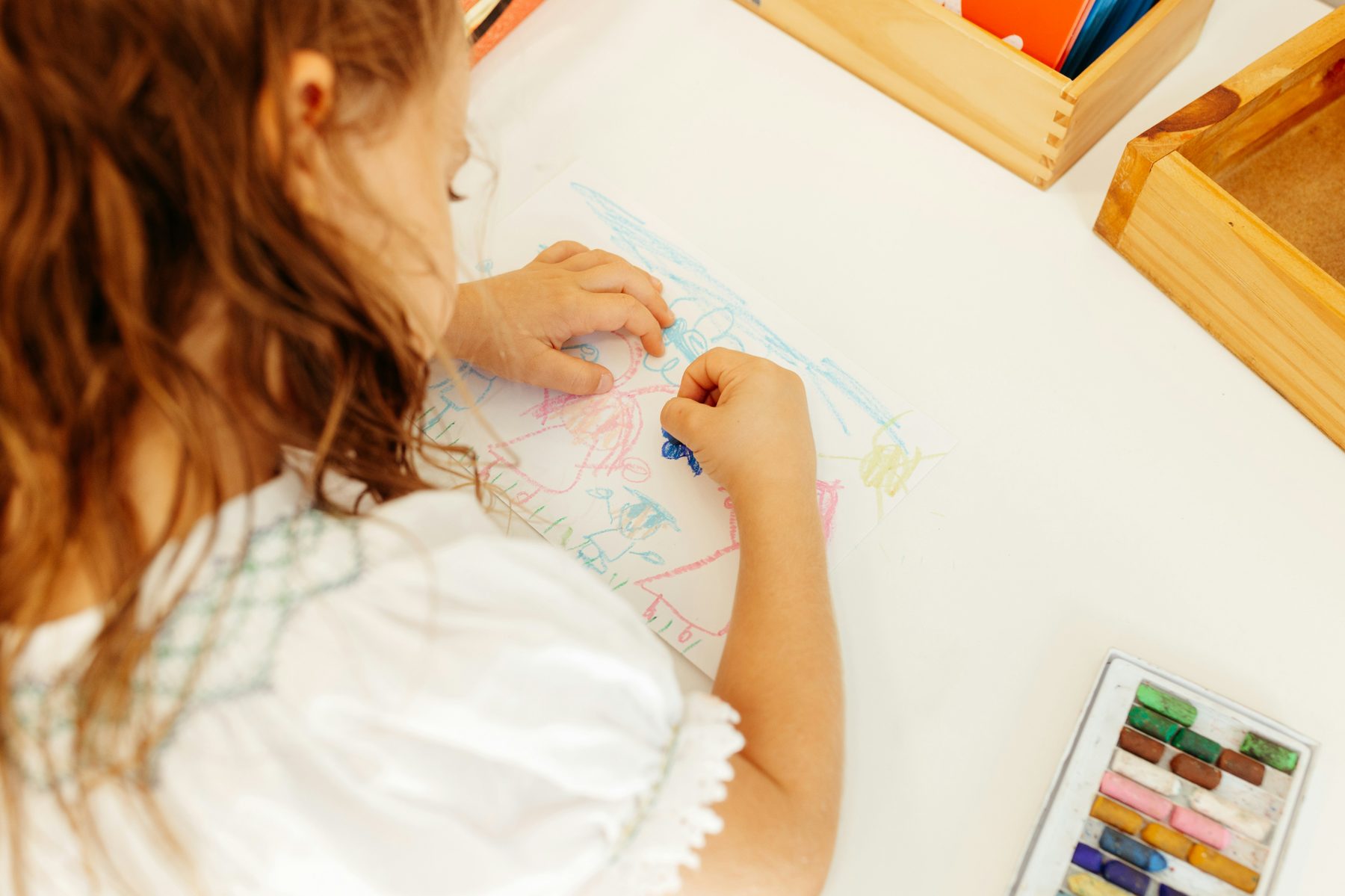A child drawing at a table strewn with paper and pens