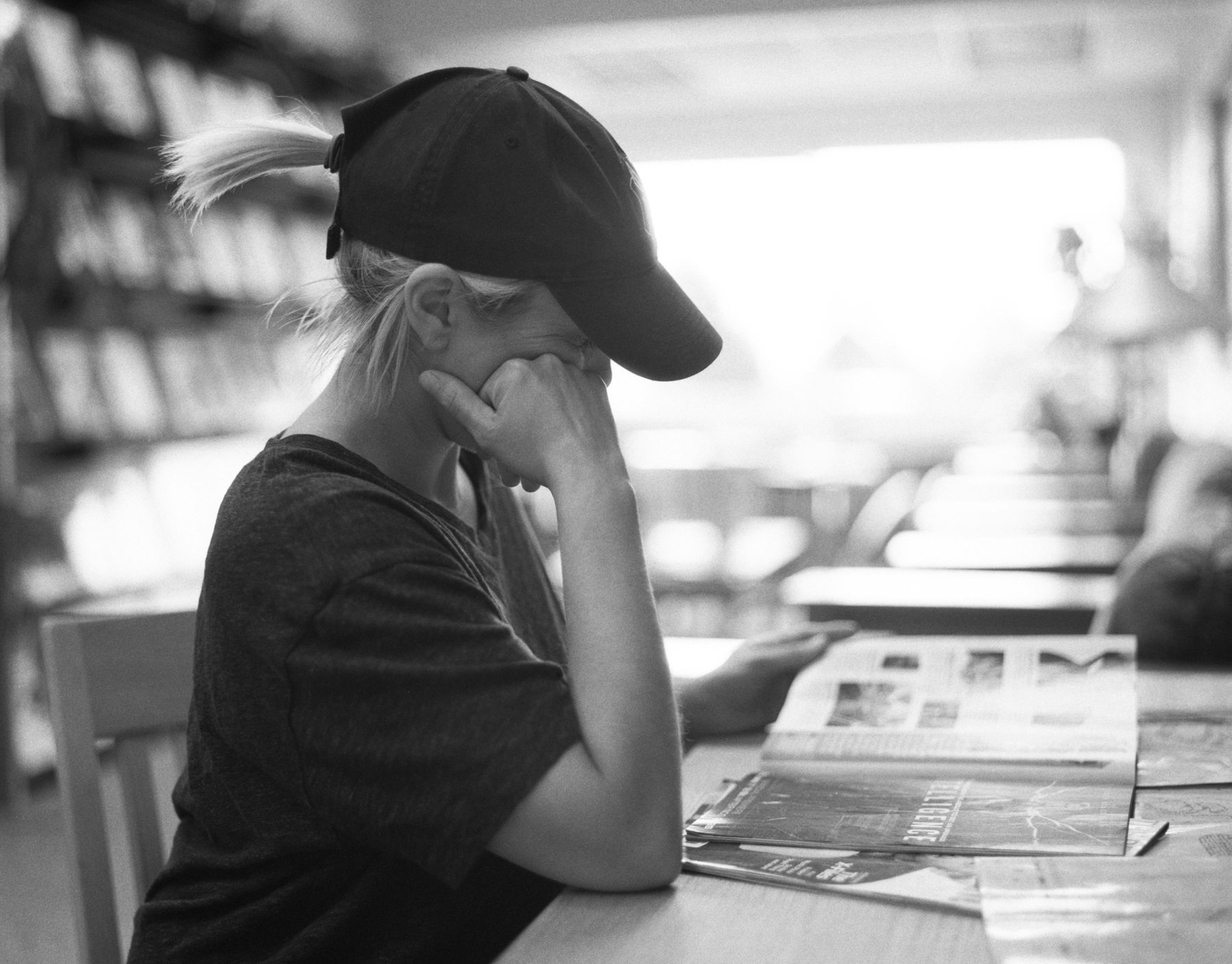A black and white frame of a teenager slumped over paperwork at a desk