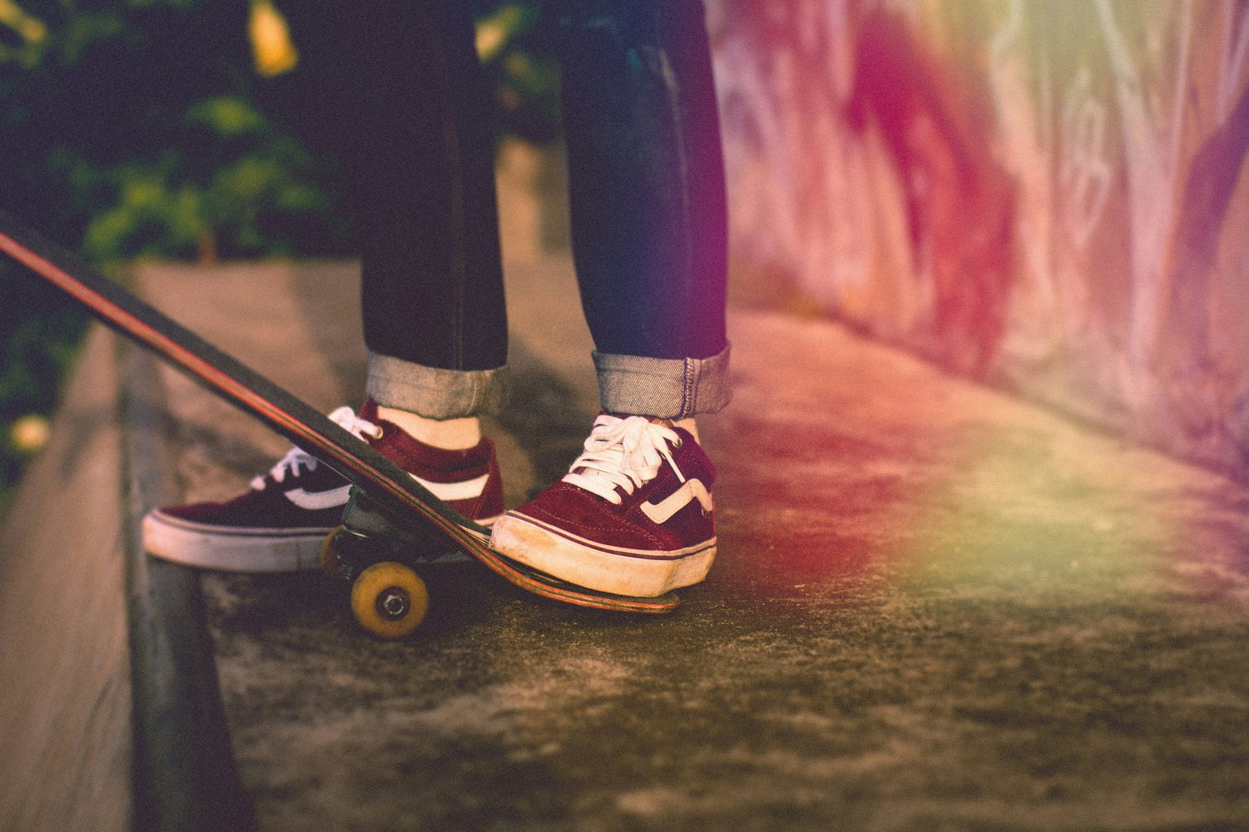 Skate shoes and a board on a lit pavement at dusk