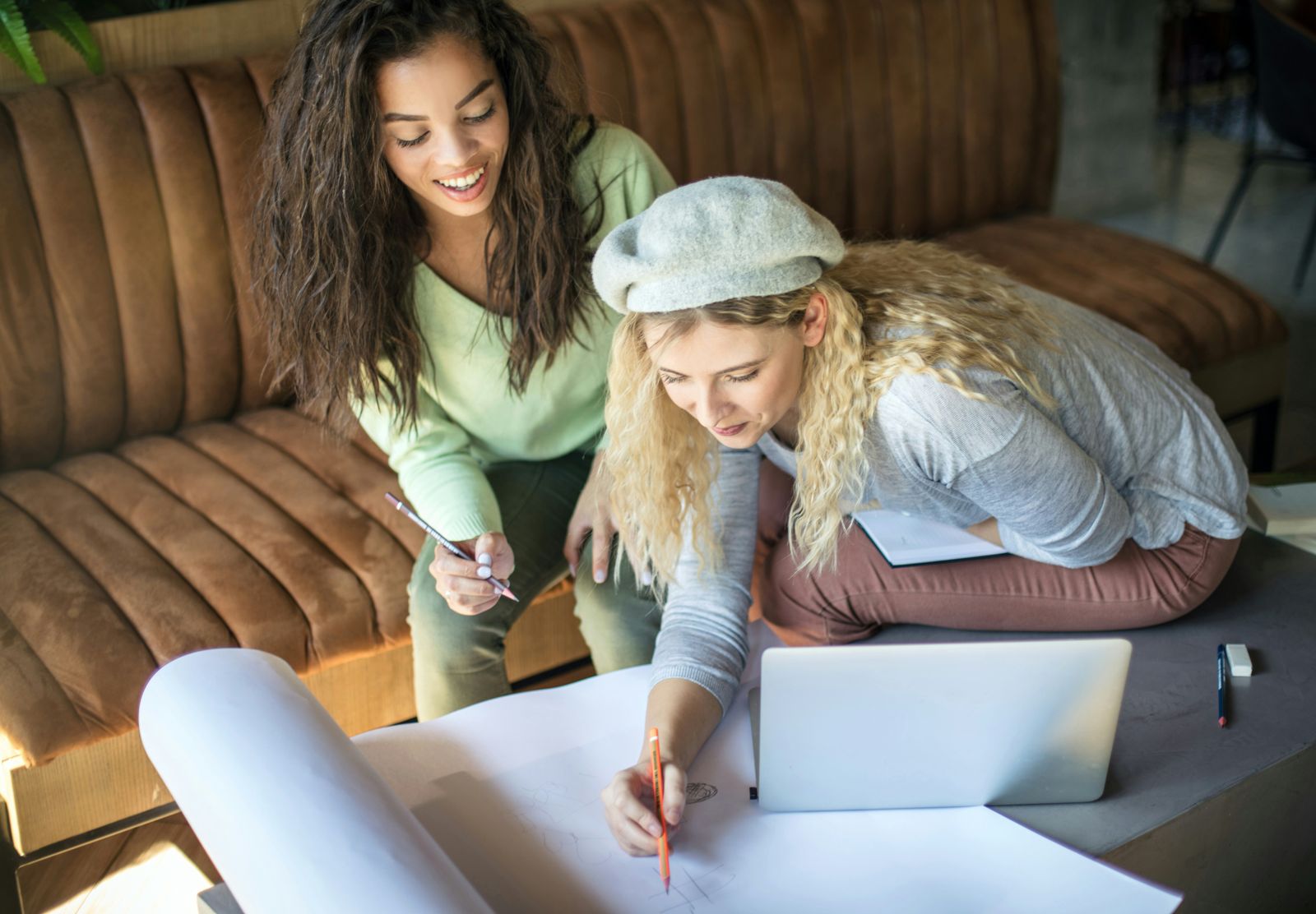 Two teenagers working together over a laptop and notes on a sofa