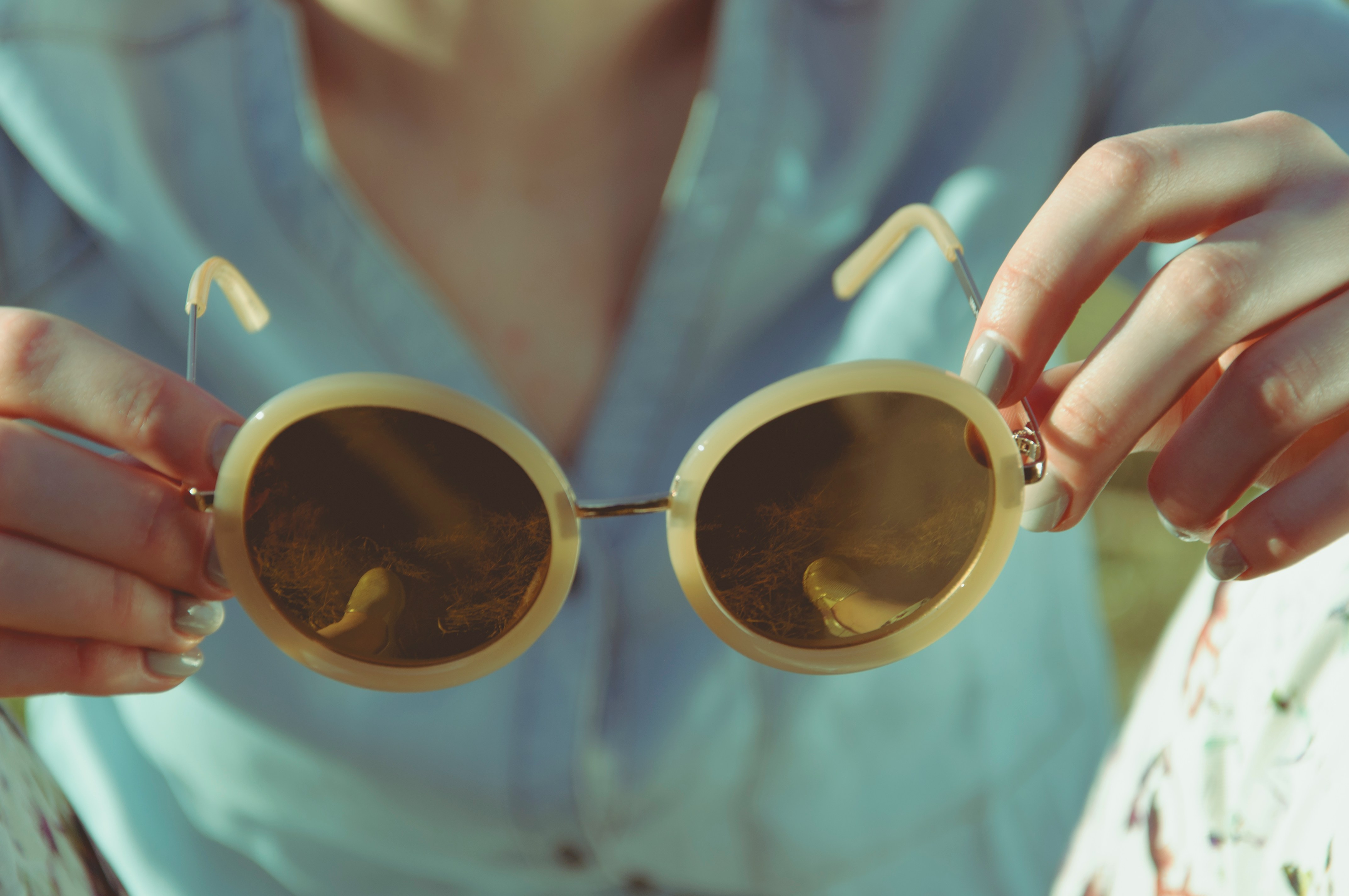 A woman holding round sunglasses in bright daylight