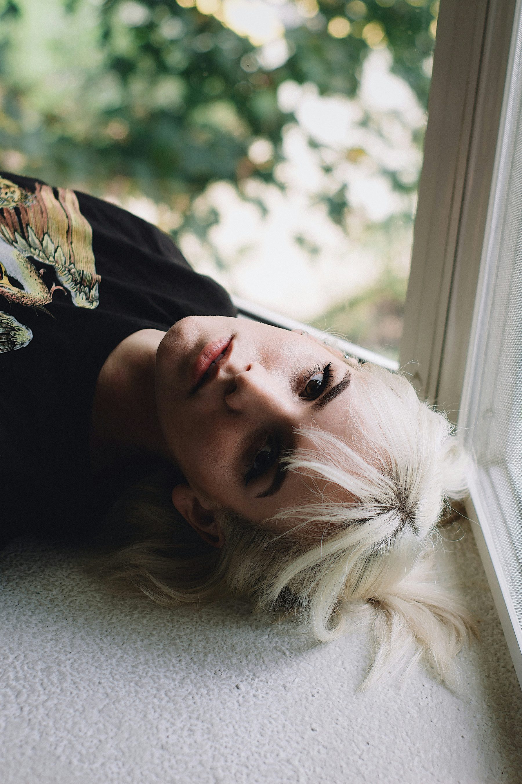 A young person lying on the floor by a window, composed and still