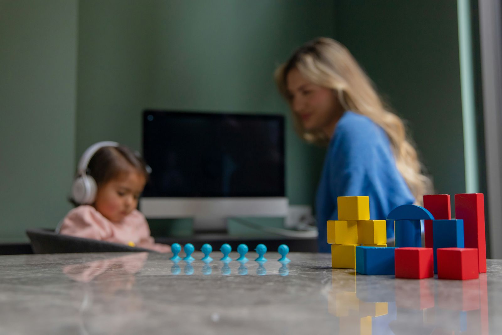 A parent working at a laptop while a small child plays with blocks nearby