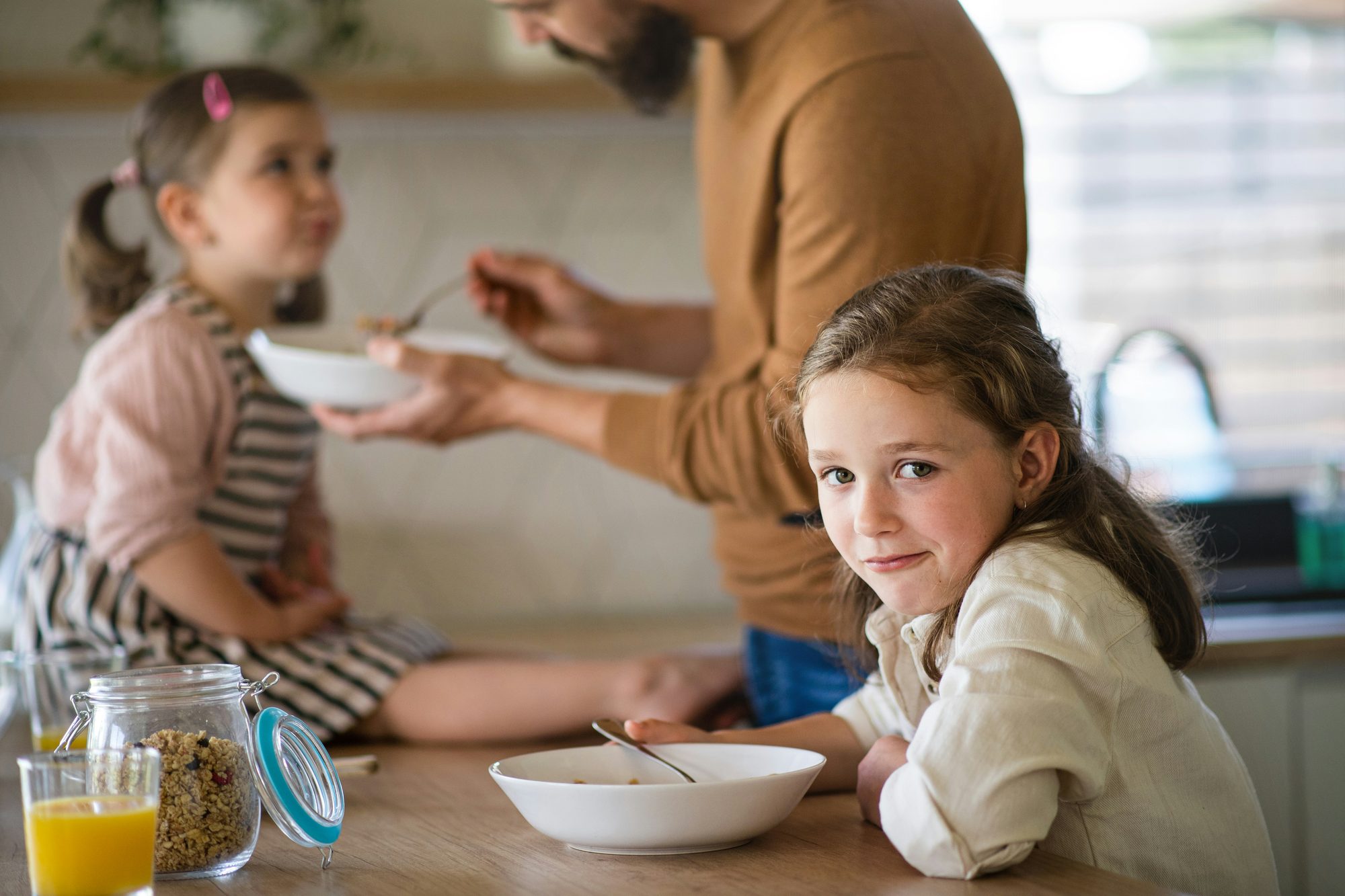 Children at a breakfast table, one looking away from their bowl mid-thought