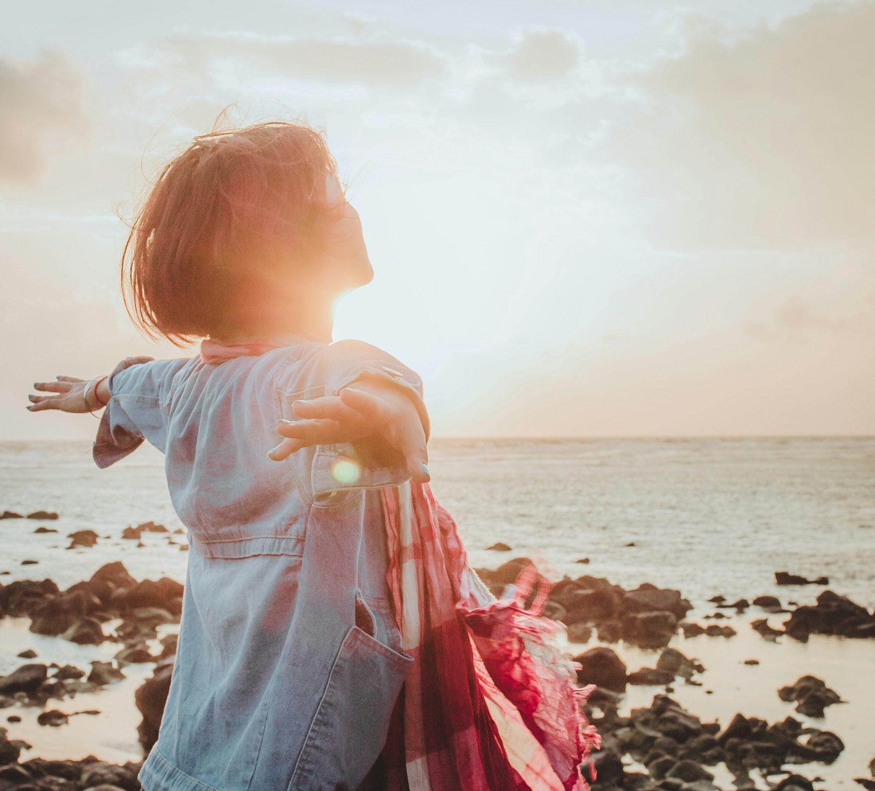 A child standing with arms out at the edge of the water at sunset