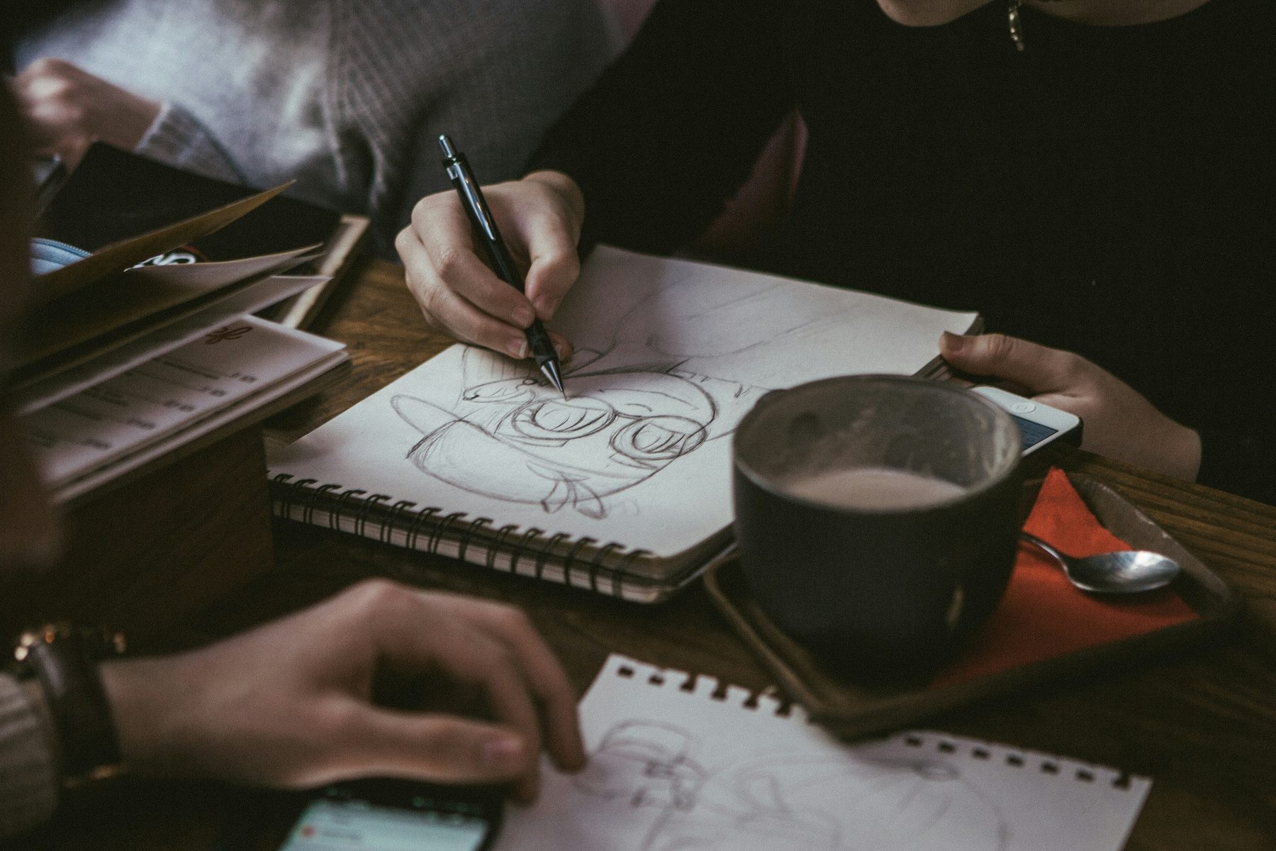 Hands writing carefully in a notebook beside a cooling drink