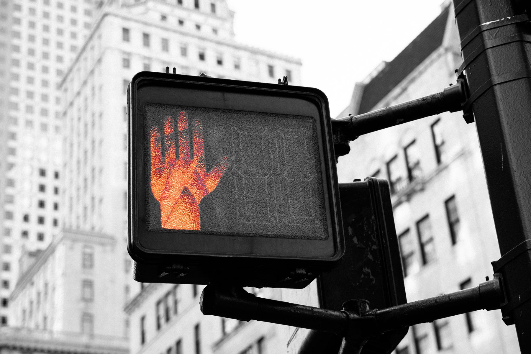 A red pedestrian stop hand glowing against a grey city block